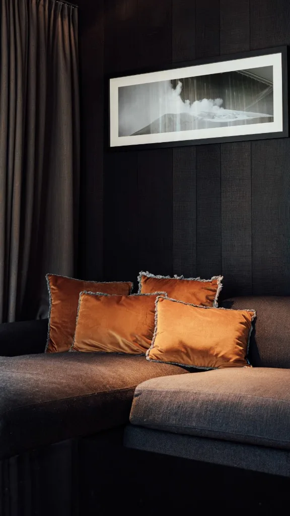 Sofa with orange velvet cushions against a dark wooden wall