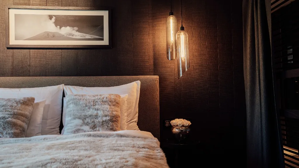 Bed with fur cushions beneath a black-and-white picture of a volcano