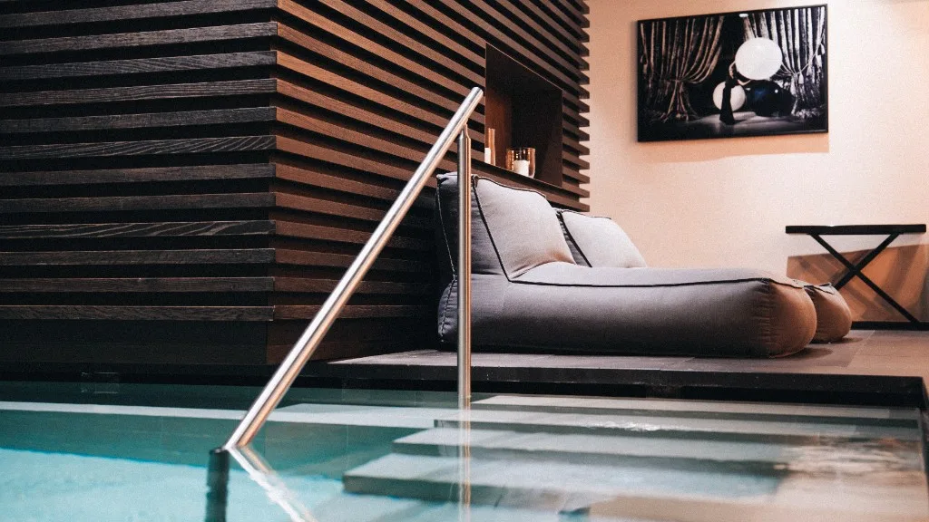 Pool with steps and lounger in front of a wooden slat wall in the spa